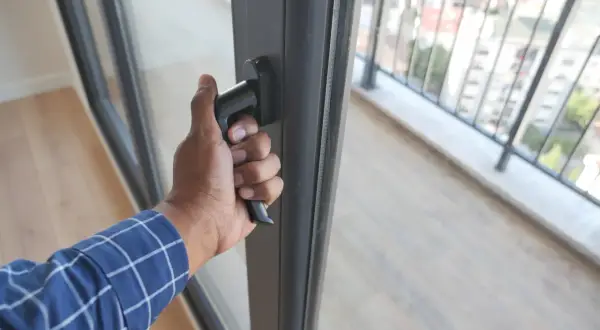 Dłoń chwyta za klamkę, wykonując regulację drzwi balkonowych. Widok na balustradę i miasto.