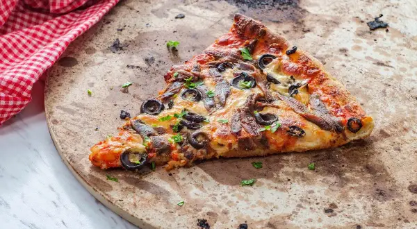 Kawałek pizzy z anchois i oliwkami na kamieniu. Dowiedz się, jak wyczyścić kamień do pizzy, by był jak nowy.