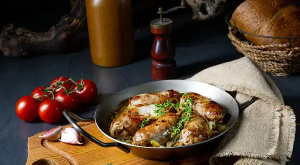 Soczysta biała kiełbasa pieczona w piwie, podana z ziołami, pomidorami i czosnkiem. Idealna na obiad.