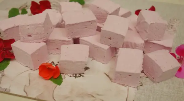 Różowe pianki marshmallow, idealne do domowego przepisu. Ułożone na wzorzystym tle, ozdobione kwiatami.