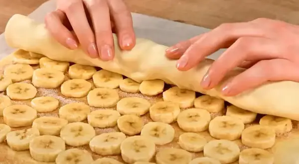 Ręce zwijają ciasto francuskie z bananem, tworząc pyszny deser.