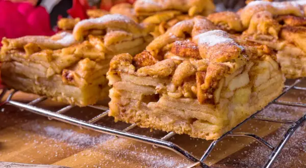 Idealne kruche ciasto na szarlotkę, z kawałkami jabłek i cynamonem, posypane cukrem pudrem, na metalowej kratce.