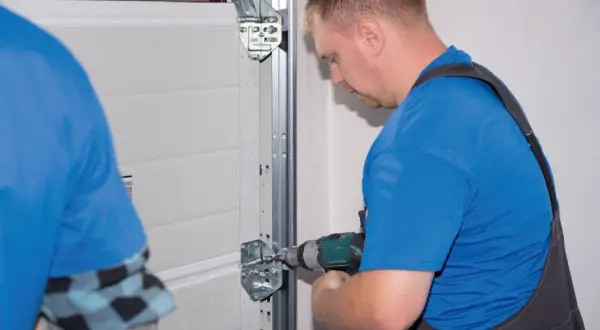 Fachowiec dokonuje regulacji bramy garażowej uchylnej, przykręcając elementy mocujące wózka jezdnego.