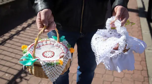 Dwie ozdobne koszyczki do święconki, jeden z koronką i kwiatkami, drugi przykryty białą tkaniną.