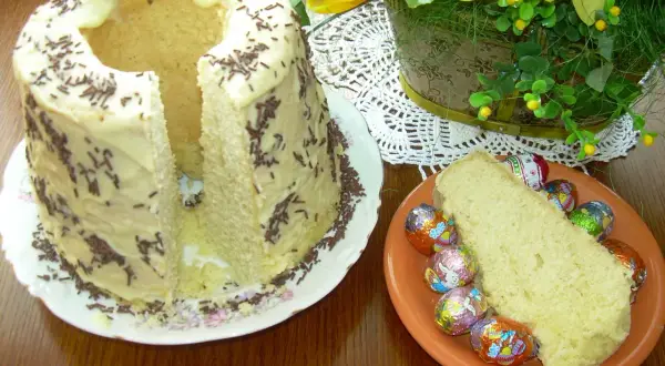Babka gotowana przepis: puszyste ciasto z lukrem i posypką, obok kawałek z czekoladowymi jajeczkami.