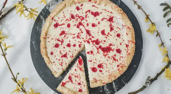 Pyszny mazurek z białą czekoladą, ozdobiony malinowym sosem, na tle wiosennych gałązek.