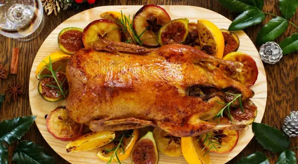 Pieczona kaczka z jabłkami, figami i pomarańczami na drewnianej desce.