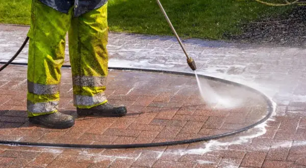 Osoba w zielonych spodniach czyści kostkę brukową myjką ciśnieniową, usuwając stare plamy z oleju.
