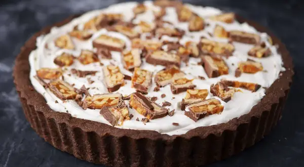 Czekoladowa tarta z kajmakiem i mascarpone, udekorowana kawałkami batoników.