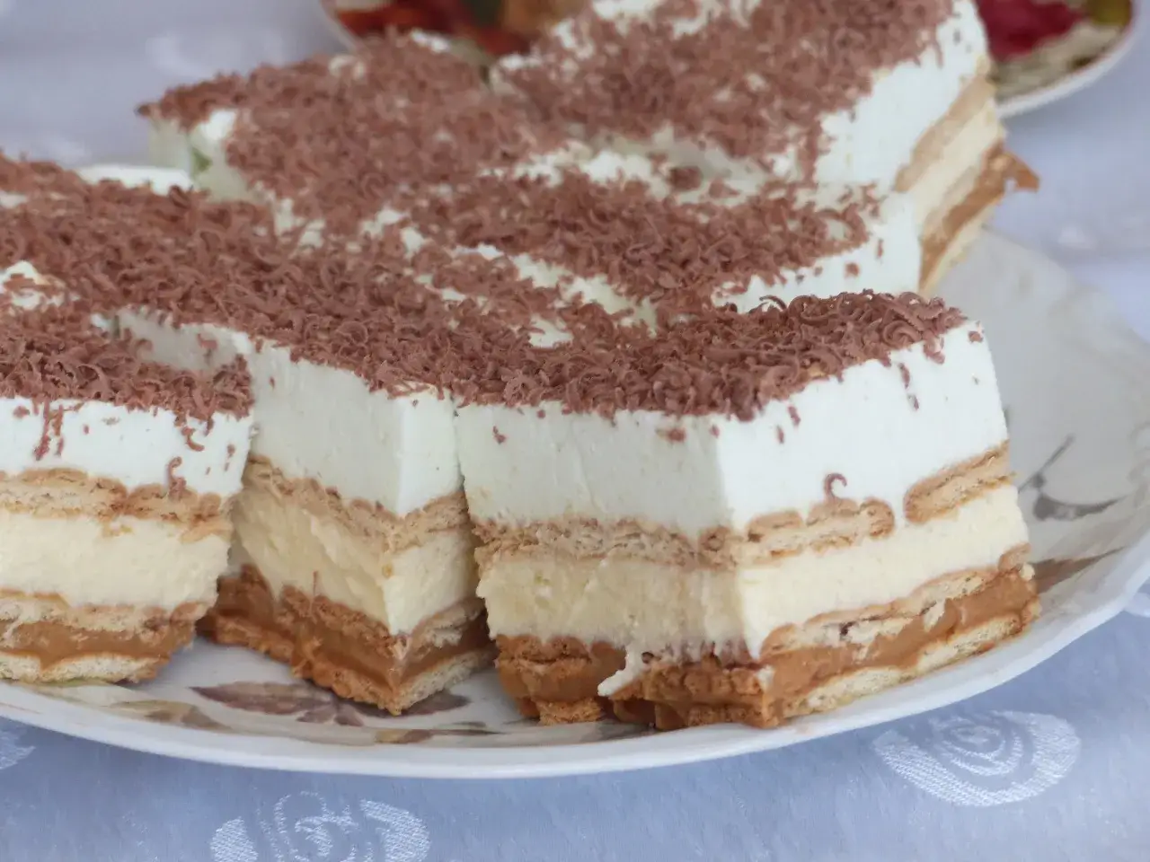 Pyszna szarlotka bez pieczenia na herbatnikach z budyniem i kremem, posypana wiórkami czekolady.