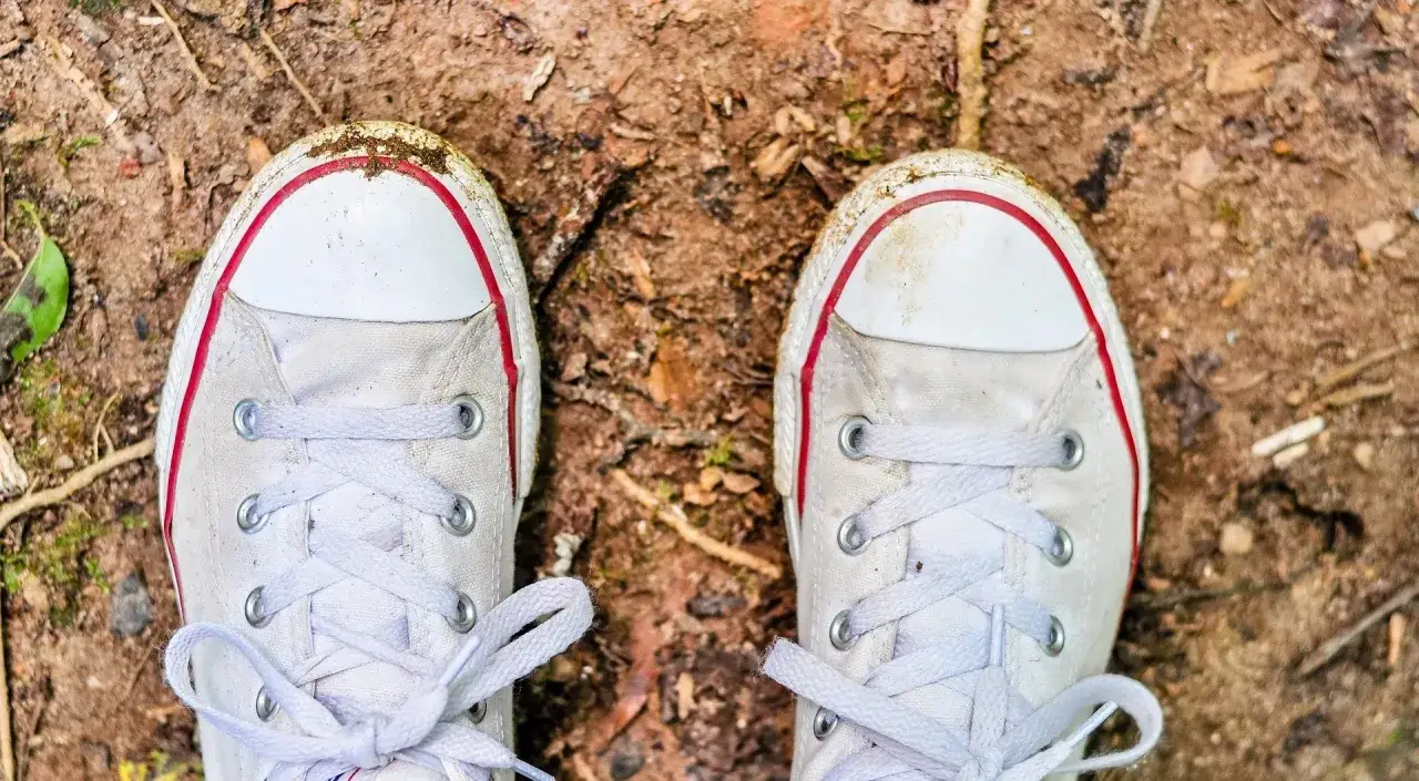 Białe trampki z czerwonymi paskami, lekko zabrudzone ziemią. Dowiedz się, jak wyczyścić białe trampki z żółtych plam, by znów lśniły.