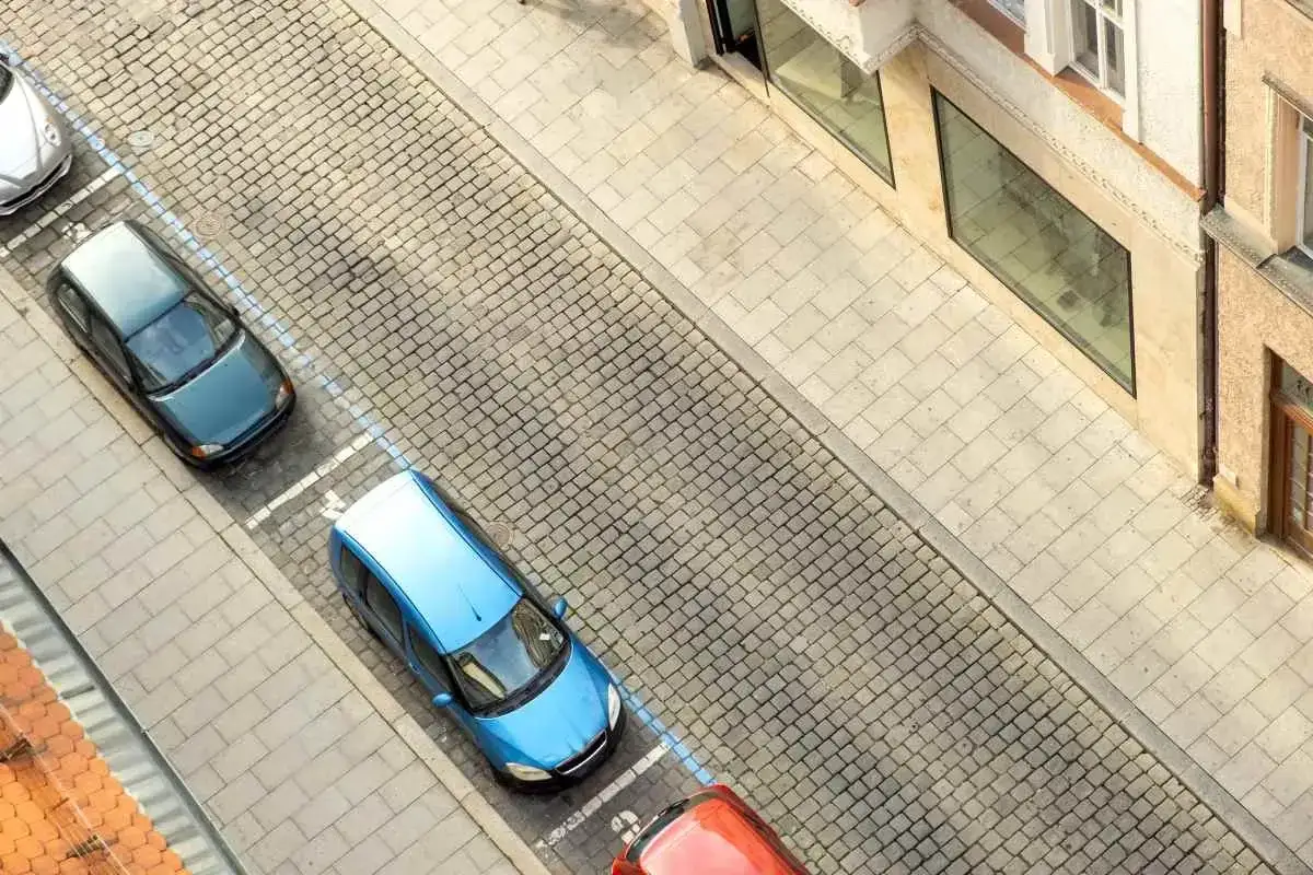 Niebieski i zielony samoch&oacute;d stoją na wyznaczonych miejscach parkingowych pod blokiem.