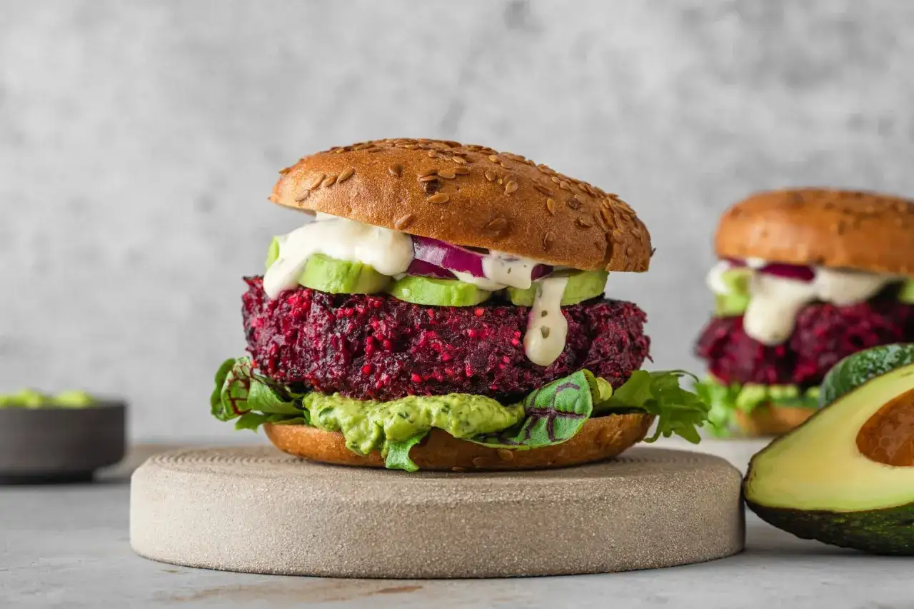 Pyszny burger z buraka z awokado, czerwoną cebulą i kremowym sosem na sezamowej bułce.
