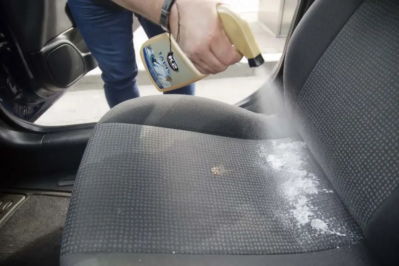 Czyszczenie siedzenia samochodowego z trudnych plam niewiadomego pochodzenia. Preparat w sprayu K2 Tapis rozpyla się na zaplamione miejsce.