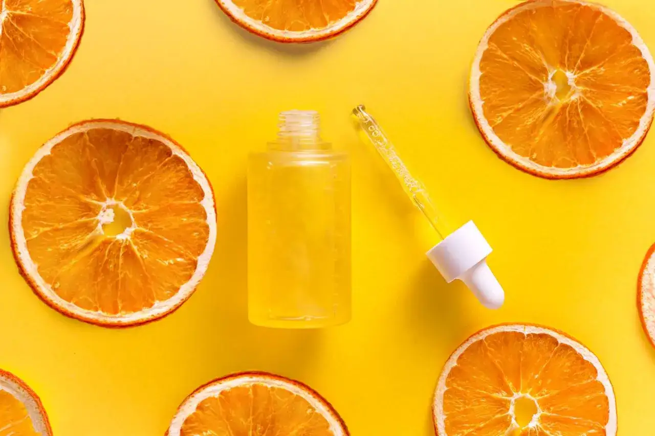 Żółte serum z pipetką i suszone plastry pomarańczy. Naturalne składniki, jak kwas cytrynowy, w kosmetykach dla rozświetlenia skóry.
