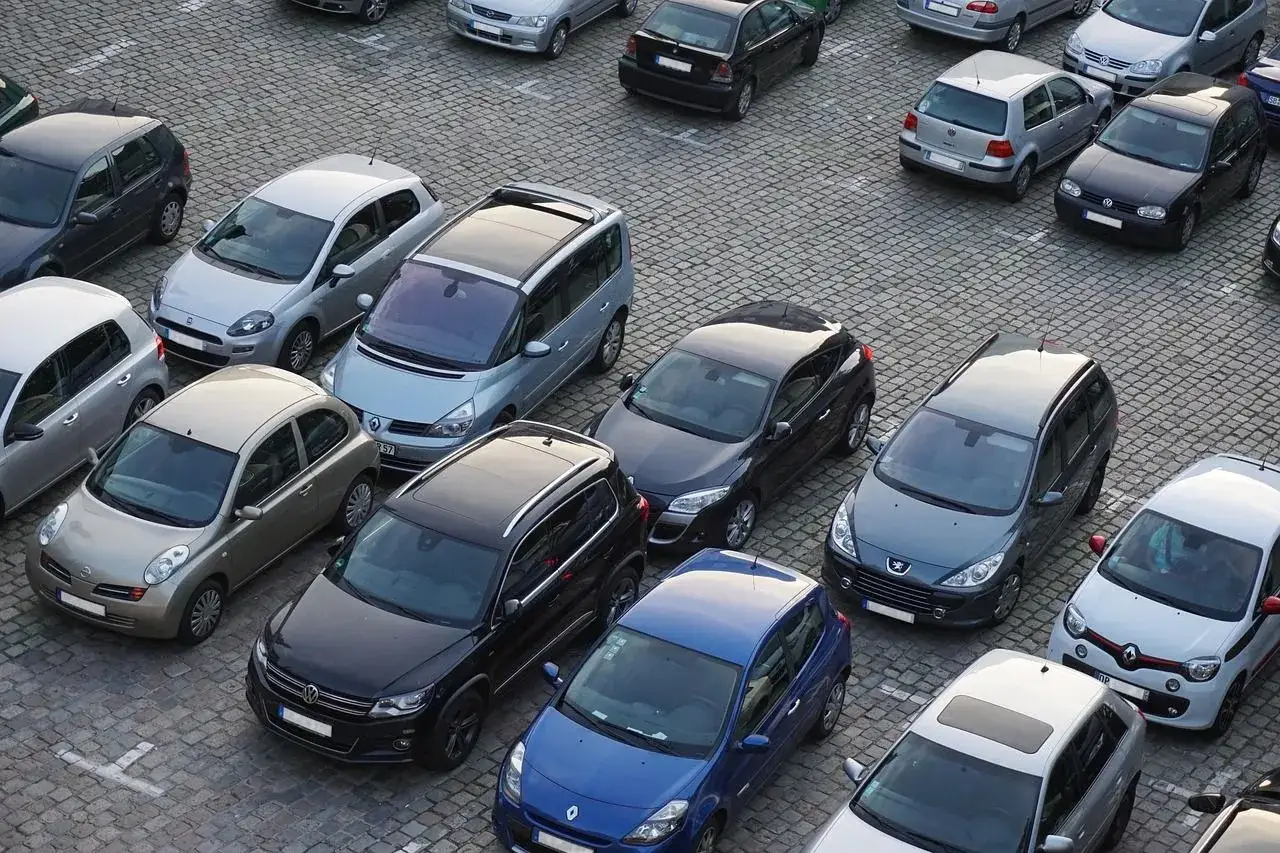 Wiele samochod&oacute;w na brukowanym placu, kt&oacute;ry służy jako prywatne miejsce parkingowe pod blokiem.