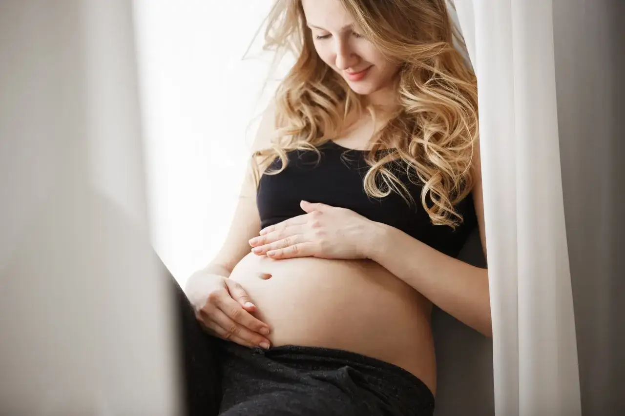 Kobieta w ciąży delikatnie dotyka brzucha. W tym okresie warto unikać kwasu glikolowego.