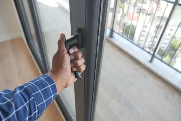 Dłoń chwyta za klamkę, wykonując regulację drzwi balkonowych. Widok na balustradę i miasto.