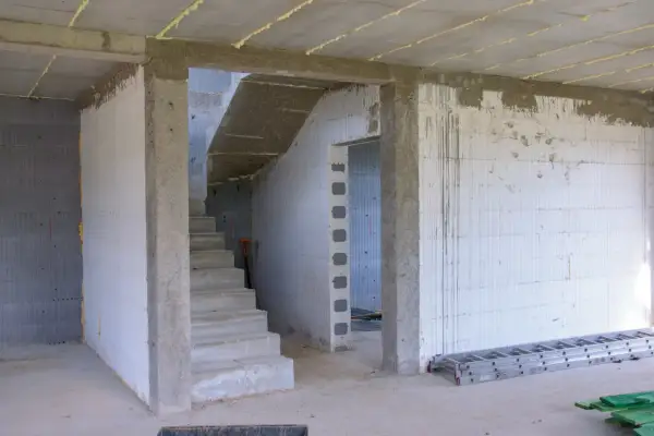 Wnętrze budowy z betonowymi schodami i pustakami. Widoczna ościeżnica stała wymiary, przygotowana do montażu drzwi.