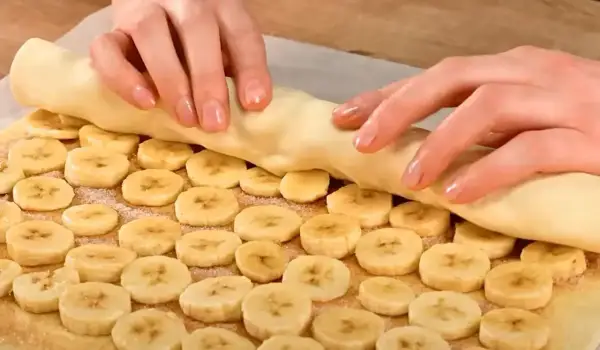 Ręce zwijają ciasto francuskie z bananem, tworząc pyszny deser.