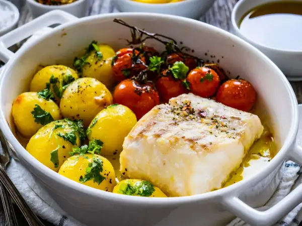 Pyszna ryba na obiad z pieczonymi ziemniaczkami i pomidorkami koktajlowymi w białej zapiekance.