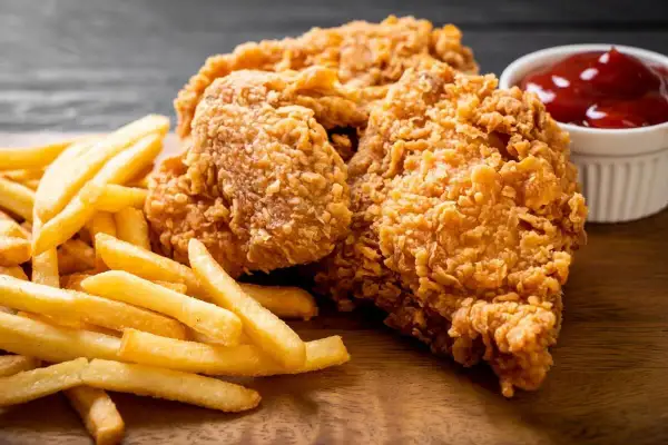 Chrupiące kawałki kurczaka w złocistej panierce do nuggetsów, podane z frytkami i ketchupem.