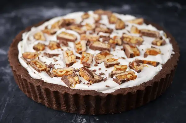 Czekoladowa tarta z kajmakiem i mascarpone, udekorowana kawałkami batoników.